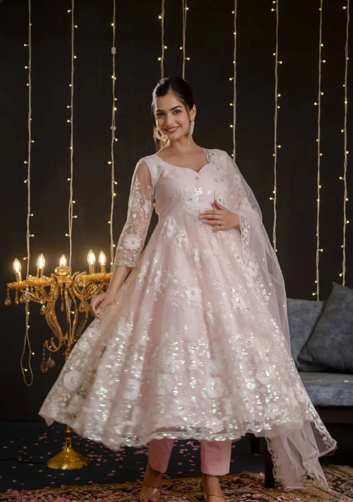 A model wearing a pastel pink embroidered net Anarkali set with matching dupatta and straight pants from Pahraav by Karishma, featuring ¾ sleeves and delicate thread work embroidery, styled for festive and wedding occasions