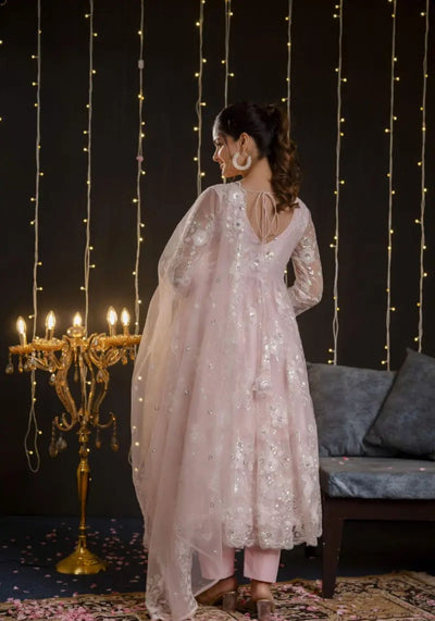 A model wearing a pastel pink embroidered net Anarkali set with matching dupatta and straight pants from Pahraav by Karishma, featuring ¾ sleeves and delicate thread work embroidery, styled for festive and wedding occasions