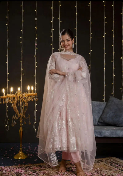 Woman in a light pink traditional outfit standing in a decorated room with string lights and a candelabra.