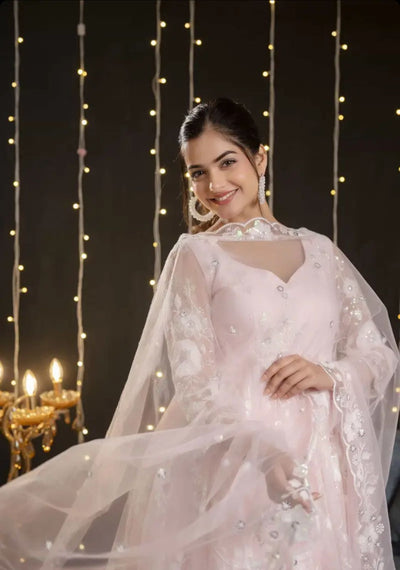 Woman in a white traditional outfit with a sheer dupatta against a string light background