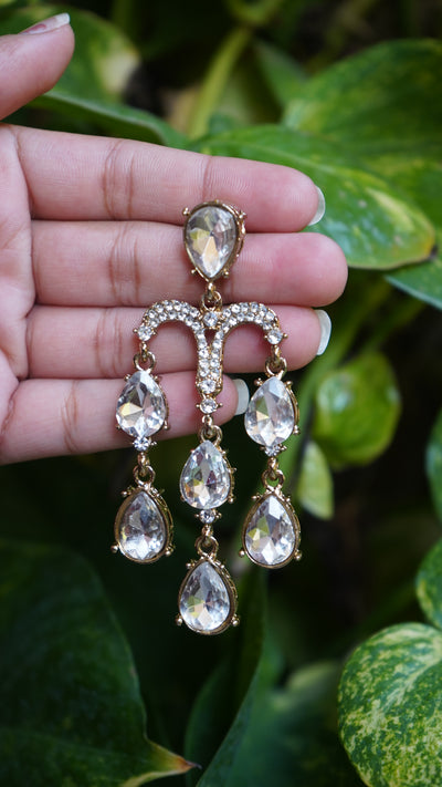 Silver-toned chandelier earrings with cascading teardrop crystals, hand-held against green leaves background – Noor Jharna by Pahraav.