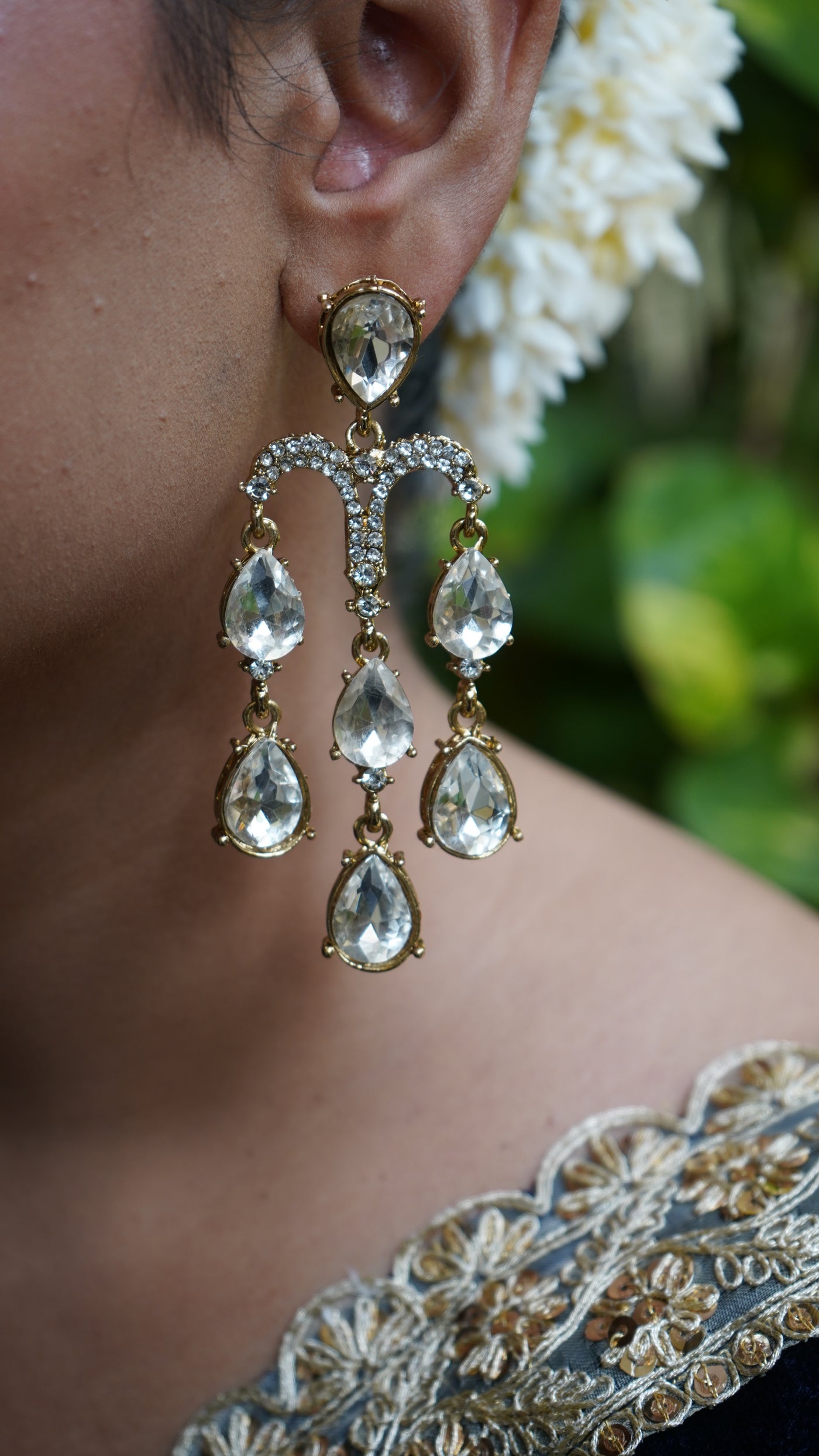 Silver-toned chandelier earrings with cascading teardrop crystals, hand-held against green leaves background – Noor Jharna by Pahraav.