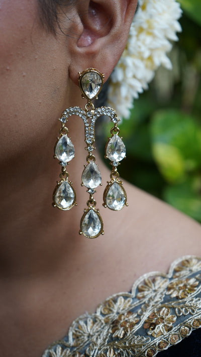 Silver-toned chandelier earrings with cascading teardrop crystals, hand-held against green leaves background – Noor Jharna by Pahraav.